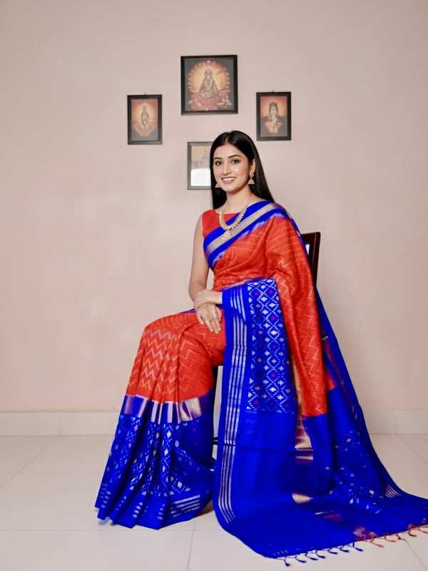 Woman wearing a traditional blue and red saree in a room with framed pictures on the wall.
