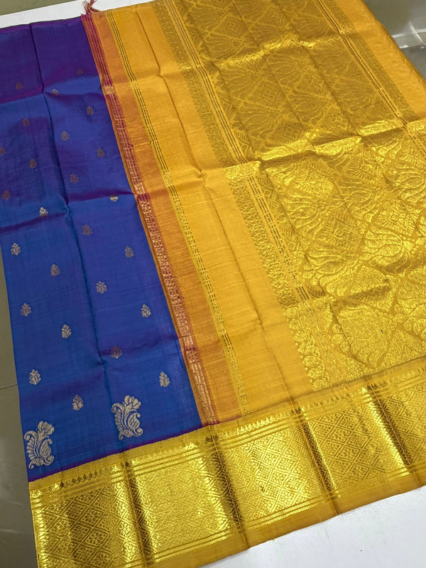 A luxury Indian silk saree with a rich royal blue body, adorned with small gold motifs, and a wide, ornate golden-yellow zari border and pallu, laid out on a white surface.