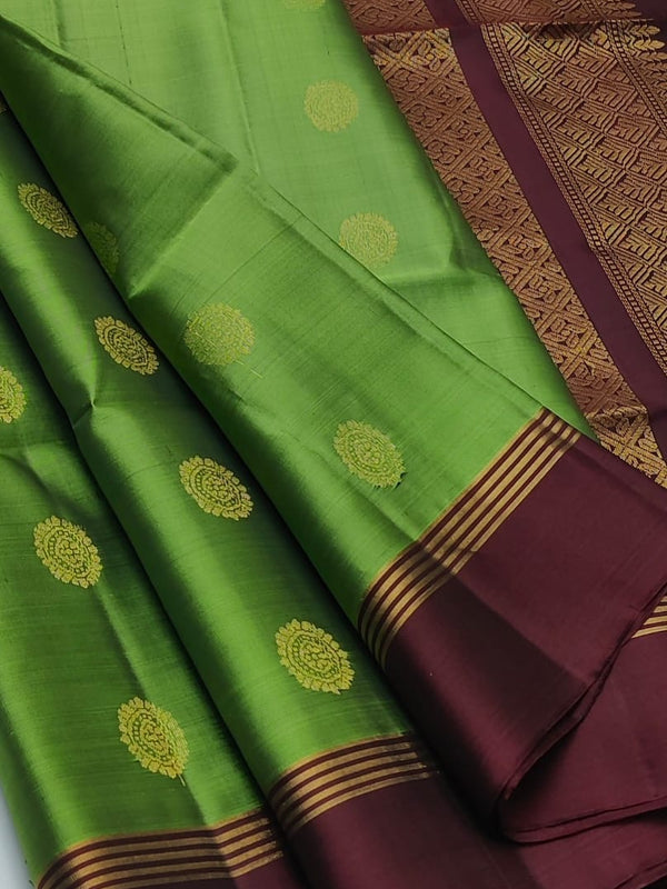 A green silk saree with gold zari motifs and a deep maroon border, draped elegantly to show its pattern and pallu.