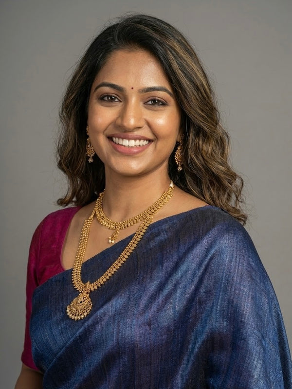 Woman wearing a blue saree with gold jewelry against a gray background
