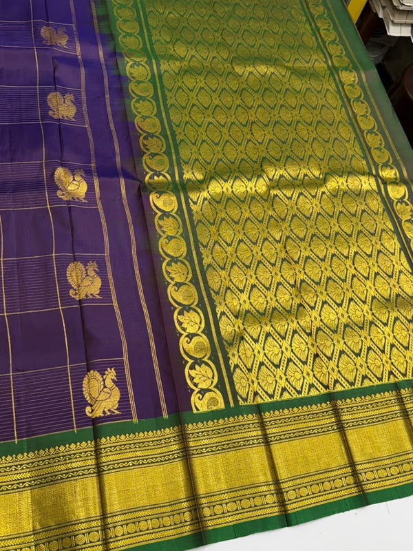 A traditional Indian silk saree displayed flat, featuring a deep purple body with gold zari motifs, a green border, and a wide gold pallu with intricate woven patterns.