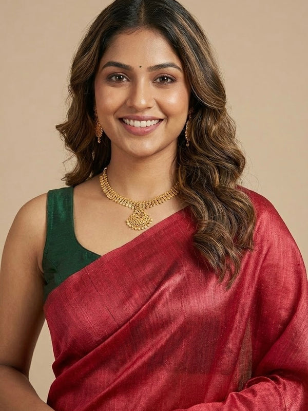 Woman wearing a red saree with a green blouse, gold jewelry, and a beige background